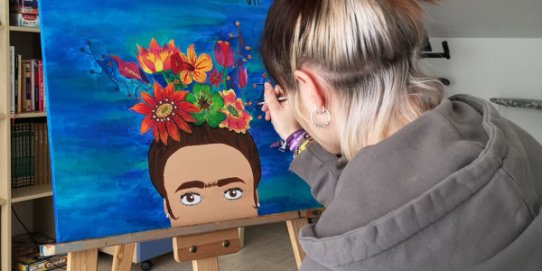 Una jove pintant un quadre que es farà arribar virtualment a les residències de gent gran.